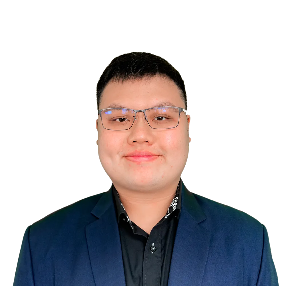 An image of Brian Tham, a young man wearing glasses and a dark suit with a black shirt, smiling at the camera
